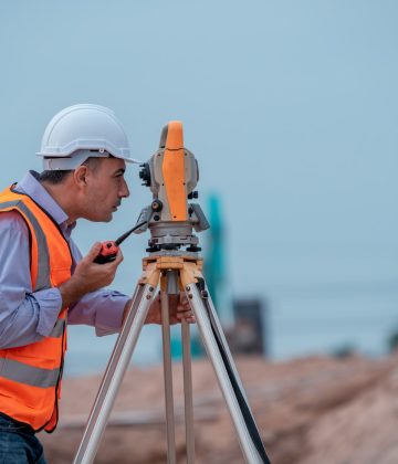 Surveyor engineers wearing safety uniform ,helmet and radio communication with equipment theodolite